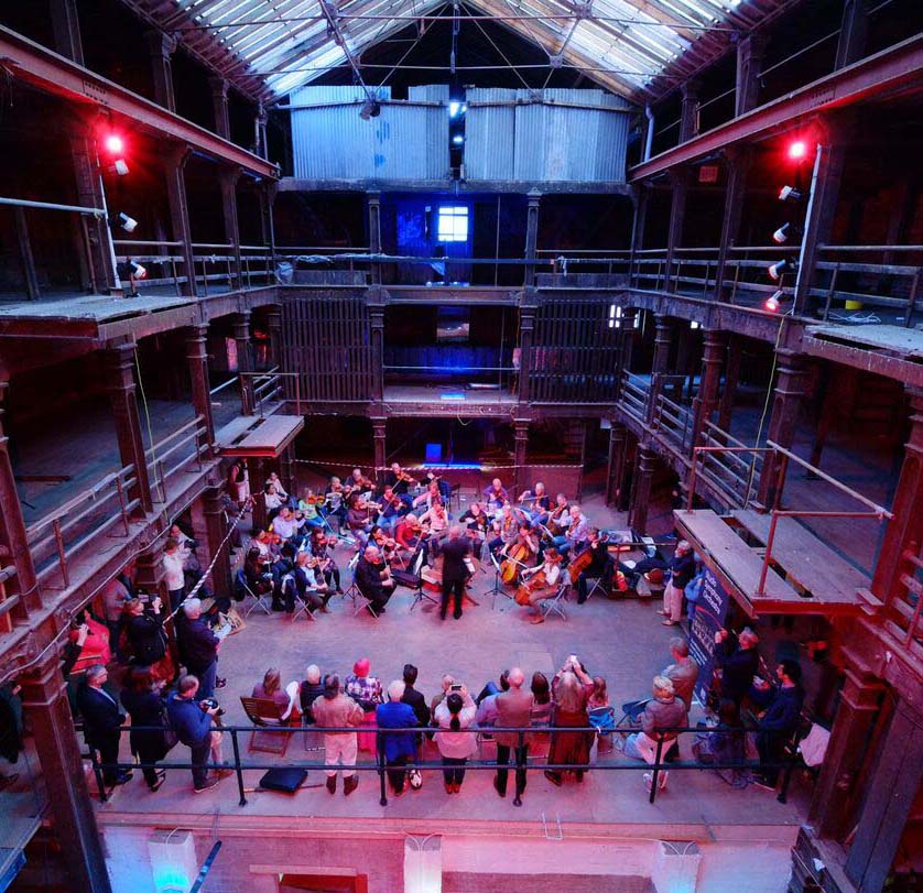 Orchestra performing to an audience in a Vistorian industrial warehouse with glazed central atrium. 